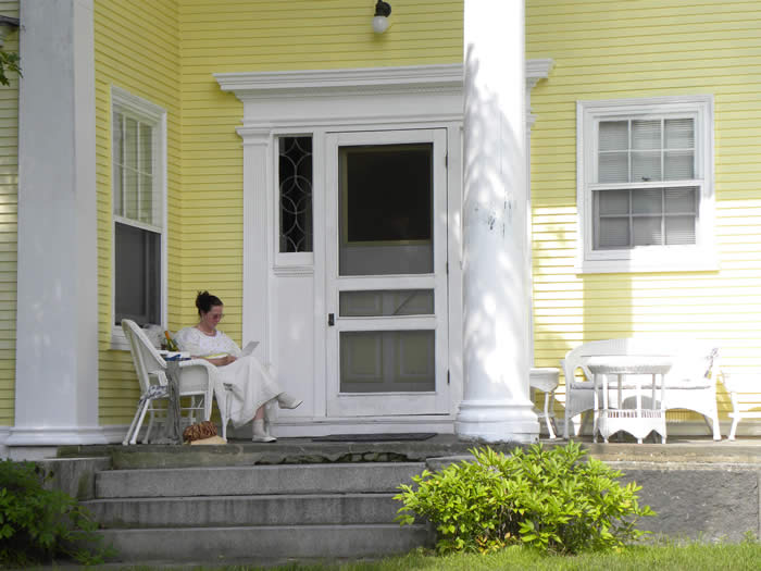 Woman in Regency costume reads on the back portico during a Jane Austen weekend