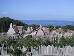 View of recreated wooden and thatch village of Plimouth with the sea beyond