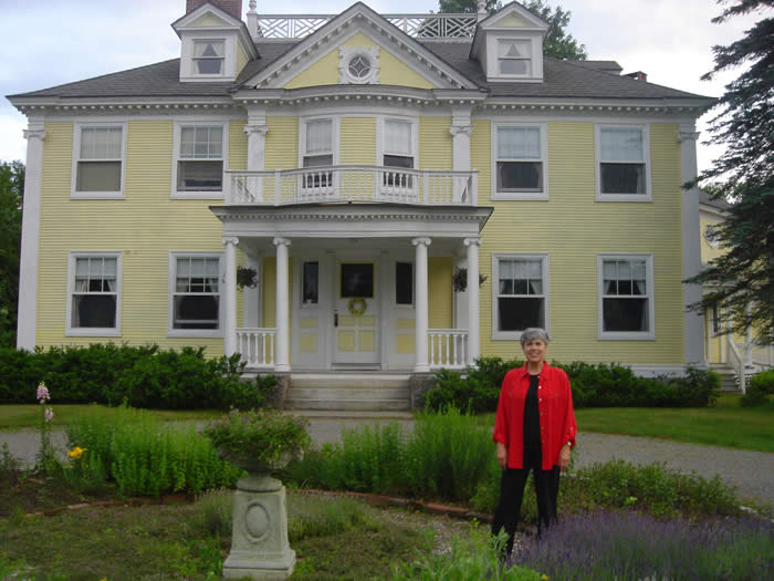 Innkeeper Suznne Boden standing in the herb garden in front of The Govenor's House, a copy of the LOongfellow House 