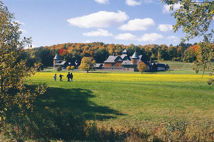 Green field with sprawling turreted building surrounded by colorful fall foliage