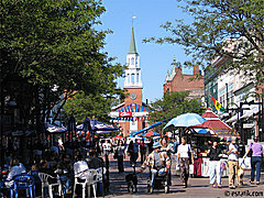 Busy pedestrain mall with colorful umbrellas, lots of peolpe and a brick church at the end: Church Street, Burlington