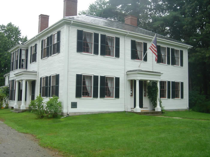 Large white colonial house with three chikneys and an American flag over the front door