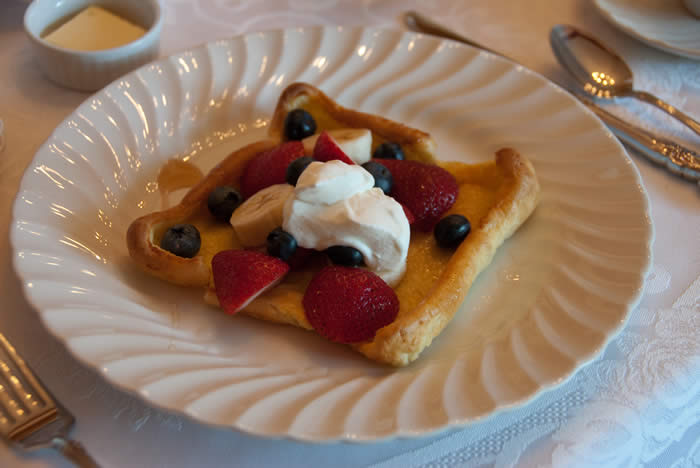 Oven-baked pancake filled with bananas, strawberries and blueberries on a white plate