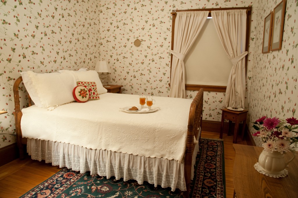 double bed with lace bed skirt in room with strawberry wallpaper