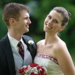 Bride holding red and white flowers and groom in suit with white carnation smile