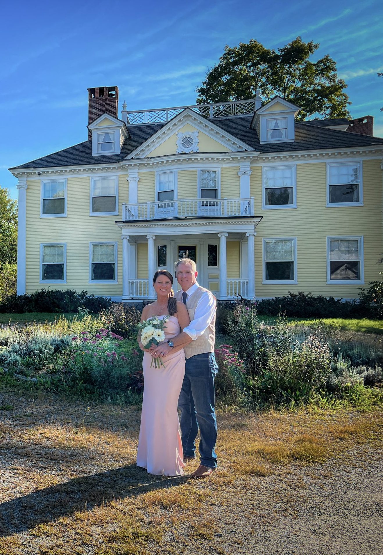 newly married couple pose in front of yellow house